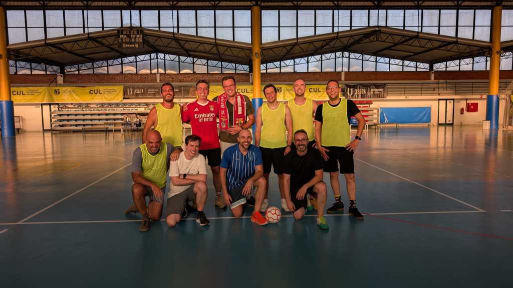 A group of eight people posing for a photo on a sports court after a football game, with some wearing yellow vests and holding a soccer ball.